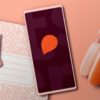телефон с логотипом Storytel и оранжевые наушники лежат на розовом столе