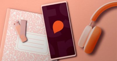 телефон с логотипом Storytel и оранжевые наушники лежат на розовом столе
